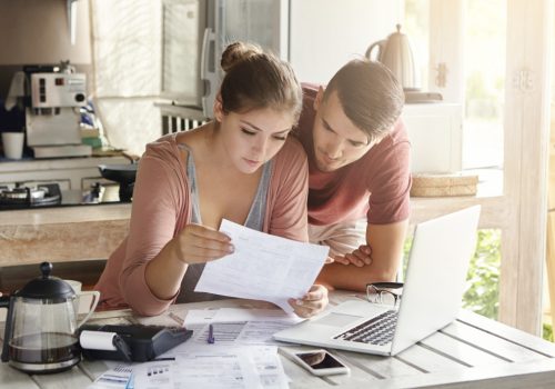 young-couple-managing-finances-reviewing-their-bank-accounts-using-laptop-computer-and-calculator-at-modern-kitchen-woman-and-man-doing-paperwork-together